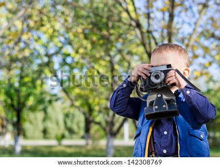 Little boy on focus taking pictures in a park with leafy tree in the background