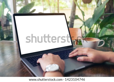 Mockup image of a woman using and typing on laptop with blank white desktop screen with coffee cup on wooden table