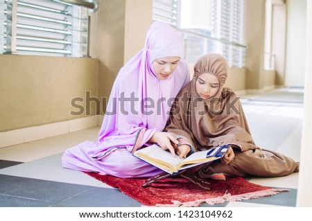 mother teach her little daughter to pray wearing muslim hijab scarf 