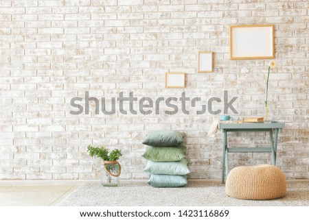 Table, pouf and soft pillows near brick wall