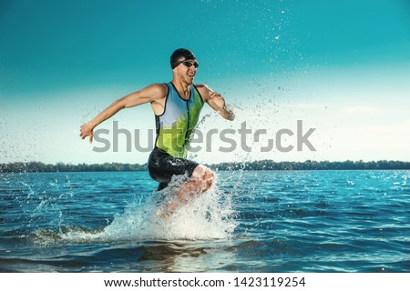 Professional triathlete swimming in river's open water. Man wearing swim equipment practicing triathlon on the beach in summer's day. Concept of healthy lifestyle, sport, action, motion and movement. Royalty-Free Stock Photo #1423119254