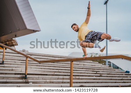 Man doing sports and training outdoors in city. Man jumping over the fence and working out hard. Parkour elements in workout.  Royalty-Free Stock Photo #1423119728