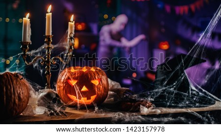 Halloween Still Life Colorful Theme: Scary Decorated Dark Room with Table Covered in Spider Webs, Burning Pumpkin, Candlestick, Witch's Hat and Skeleton. In Background Silhouette of Monster Walking By