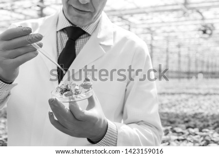 Black and White photo of Midsection of male biochemist using pipette on seedling in petri dish at greenhouse