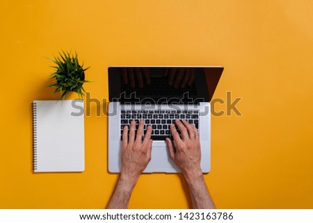 flat lay of male hands typing on laptop keyboard on yellow background