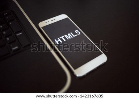 Programming language HTML5 for mobile development, concept. Smartphone near the laptop keyboard, the programmer's workplace