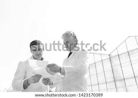 Black and White photo of Mature male biochemists discussing over documents against clear sky
