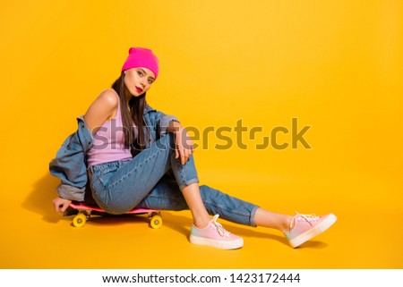 Full length side profile body size photo beautiful she her lady weekend vacation sporty sitting own skate board not smile wear casual jeans denim jacket shoes pink hat isolated yellow vivid background