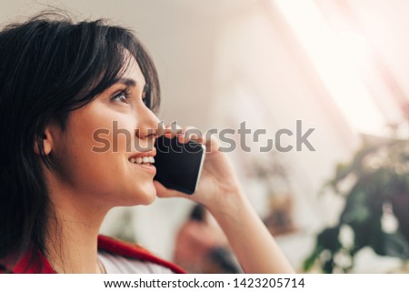Bright sunlight picture of brunette buisnesswoman talking on phone. Sitting in coworking room and look at window. Online conversation