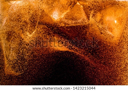 Close up view of the ice cubes in dark cola background. Texture of cooling sweet summer's drink with foam and macro bubbles on the glass wall. Fizzing or floating up to top of surface. Royalty-Free Stock Photo #1423215044