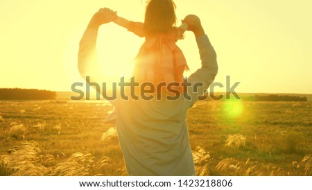Dad dancing on his shoulders with his daughter in sun. Father travels with baby on his shoulders in rays of sunset. child with parents walks at sunset. happy family resting in park. family concept