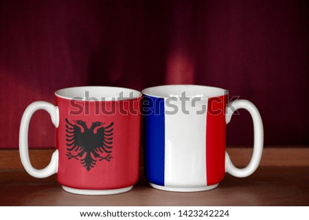 France and Albania flag on two cups with blurry background