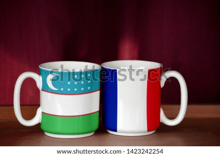 France and Uzbekistan flag on two cups with blurry background