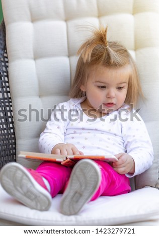 Sweet litlle baby girl sitting and reading the book. Outdoor photography