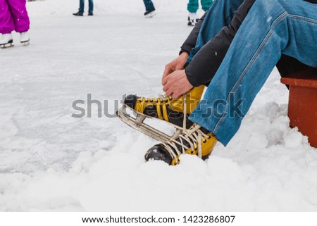 Hands tie a long string on the yellow leather boot of the modern skate. Around is loose snow
