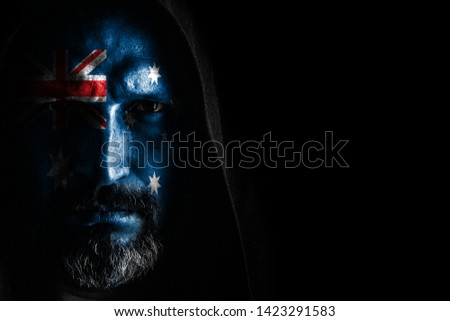 A brutal man with a gray beard, with the flag of Australia on his face, in a hood with sharp shadows on a black background. Copy space