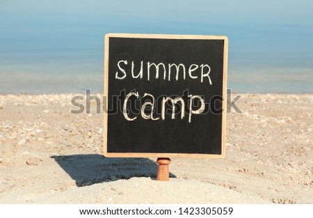 Small chalkboard with text SUMMER CAMP on beach near river