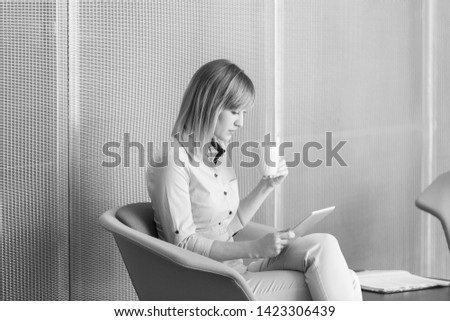 Black and White photo of Businesswoman looking at digital tablet while having coffee in office