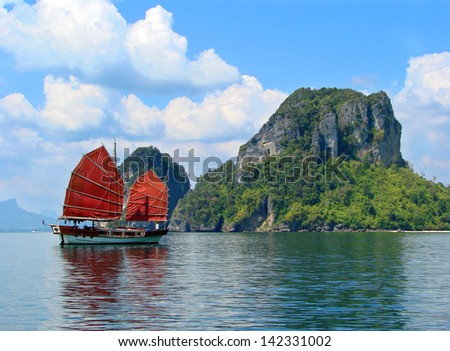 Exotic asian ship with red sails on the background of the island and the sky. The picture was taken near the Phuket island, Thailand