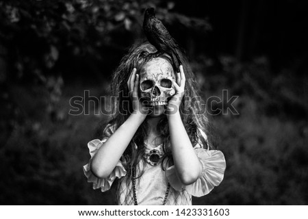 Young girl with wearing a Victorian dress and messy hair holding a skull over her face.