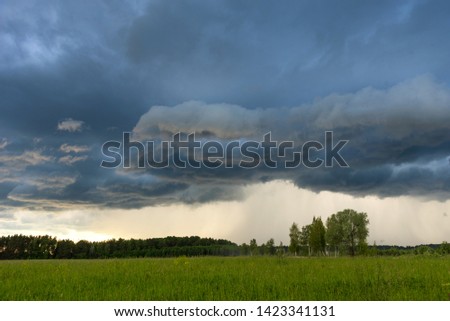 Rural landscape green field with dramatic sky. Grey dark sky before thunderstorm in summer