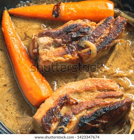 Fried pork with carrots and onion sauce in a pan, top view, close-up - French cuisine