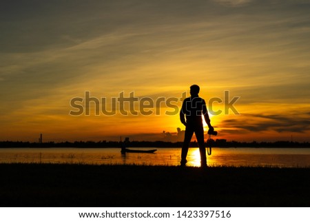 The silhouette of the photographer a man stood over the mountains and rivers that had the sun shining in the evening, holding a camera in his hand