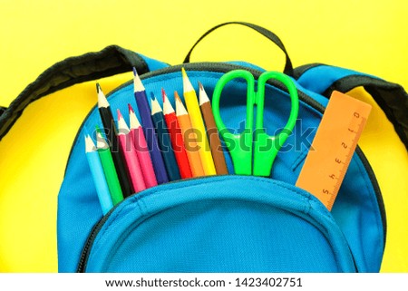 Blue Backpack with different colorful stationery on yellow background. Back to school