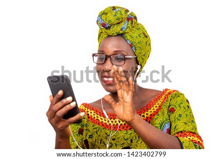 beautiful african adult woman dressed in loincloth and green scarf with glasses, takes pleasure communicating with headphones, in his mobile while smiling