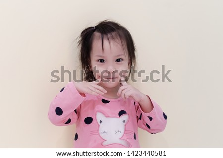 Soft focus and Closeup Portrait adorable little Asian girl 3 year old smiling. Kid using finger point to her cheek to making happy face. Happy face of Asia kid. Concept of happiness kids, Cheerful.