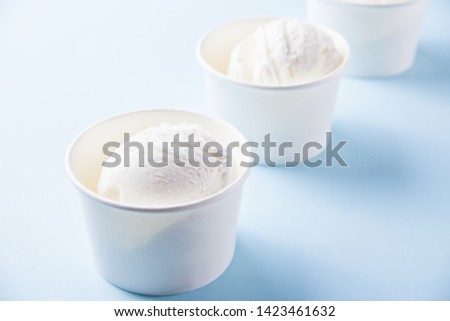 Row of paper bowls of vanilla ice cream on the blue background.