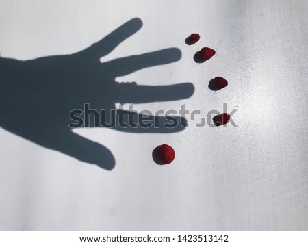 Five fresh small red strawberries and shadow of hand with five fingers 