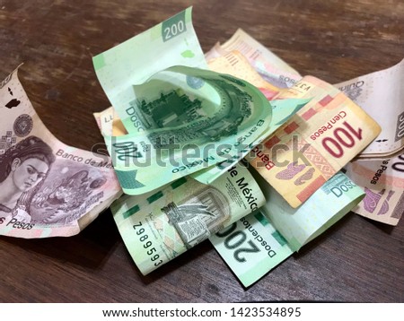 Many mexican pesos bills spread over a wooden desk inside a small business office