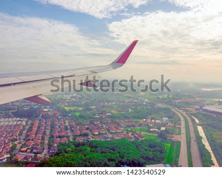 wings of airplane during the flight look from the passenger window. There are white clouds in the blue sky. Low flying above the ground, overlooking the clear city streets below Bangkok, Thailand