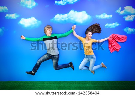 Couple of happy young people are running on a green meadow over blue sky.