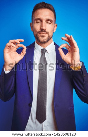 Vertical angle picture of young handsome business man over blue isolated background relax and smiling with eyes closed doing meditation gesture with fingers. Yoga concept.