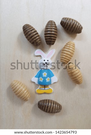 Abstract Аrt in the Photo: the figure of a cheerful Bunny between decorative wooden beads on a light background of plywood