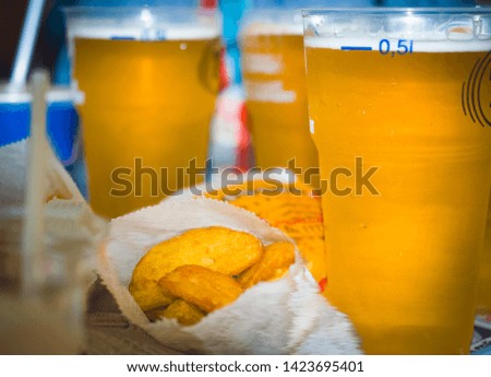 Fast food: Several plastic glasses with cold beer standing next to traditional french fries. Selective focus.