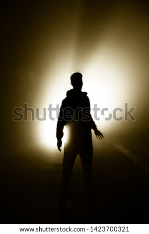 The man standing alone silhouette the darkness, abstract mysterious sci fi fantasy concept, bright light rays from behind, person alone in dark background