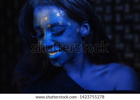 Young beautiful girl with blue face painting posing in studio on black background