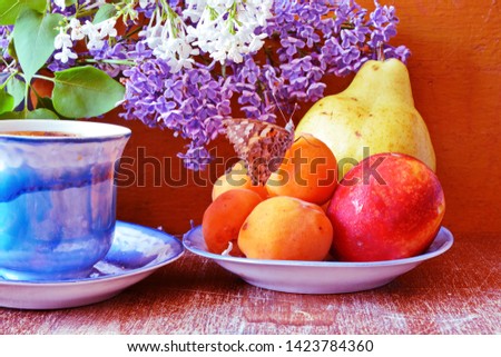 Still life with garden lilac and fruits. Bouquet of flower of lilac in a bowl, ripe pears, plums, peaches on dish with red butterfly and pattern cup of tea on an old vintage wooden background. Closeup