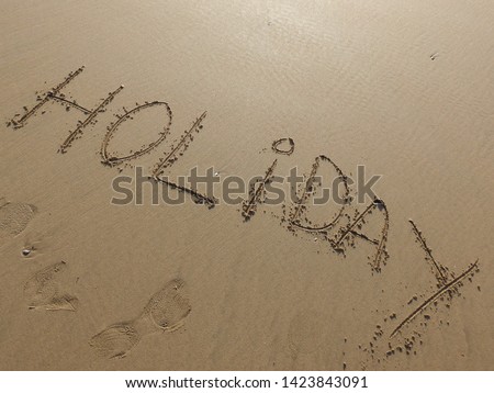 " holiday " word is written  by hand  on the beach sand .