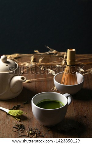 A cup of hot matcha green tea  with tea pot accessories decorated on wooden table, low light mood and tone