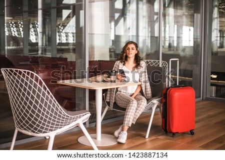 Beautiful business woman with smartphone waiting for her flight in an airport's cafe.
