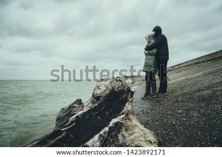 The guy with the girl walk along the embankment in rainy weather and take pictures