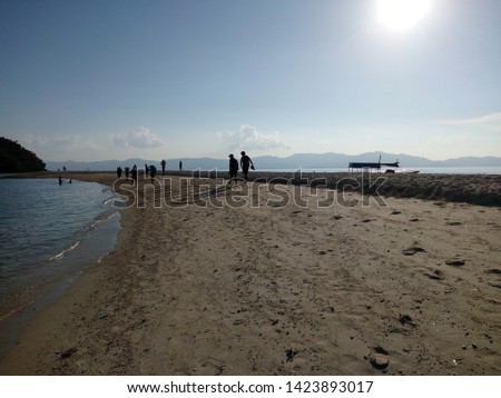 Picture of a beach with a sand bar where people walk to reach the little island from afar. The photo was taken during the summer vacation on an island with white sand.