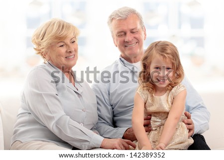Grandparents laughing with granddaughter on couch at home