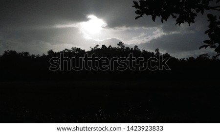 A picture of the sunshine trying to peep out of the dark clouds above the silhouette of a mountain underneath. This photo of a natural process was taken after a heavy rainfall in a provincial town. 