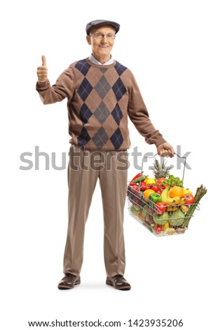 Full length portrait of a cheerful senior man with a full shopping basket showing thumbs up isolated on white background