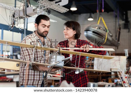 Diligent cheerful couple enjoying their hobbies - modeling light airplanes in aircraft hangar